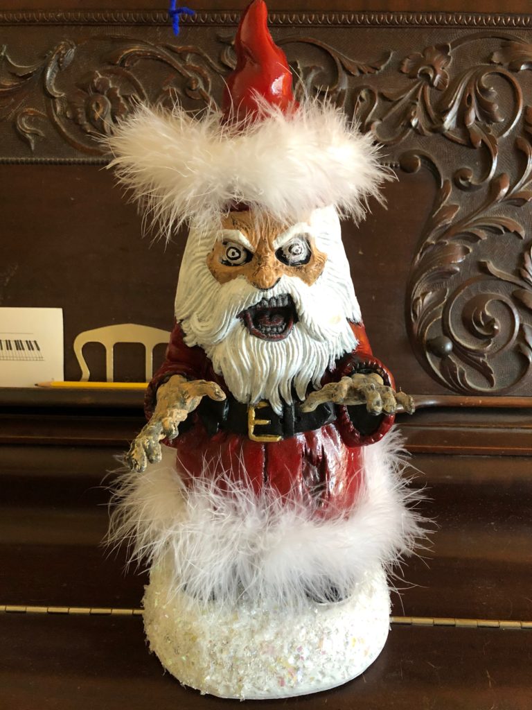 Garden gnome painted and dressed as a zombie Santa Claus.